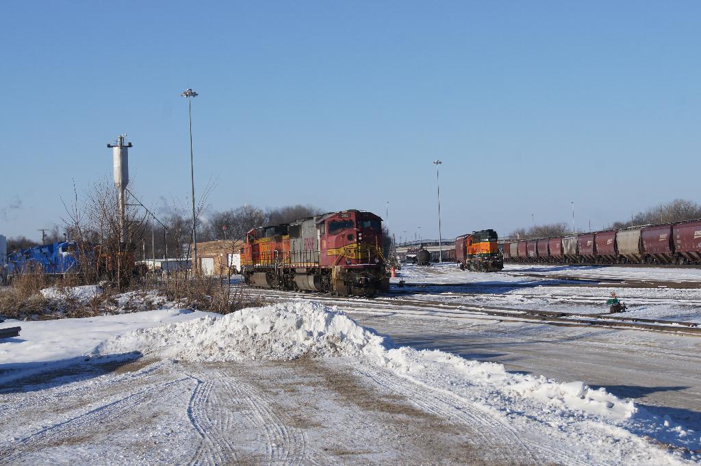 Eine Lokomotive vorne mit einem Eisenbahnwagen auf der rechten Seite, auf Schienen geparkt mit Schnee auf dem Boden, trockenen Bäumen und einem Strommast im Hintergrund.