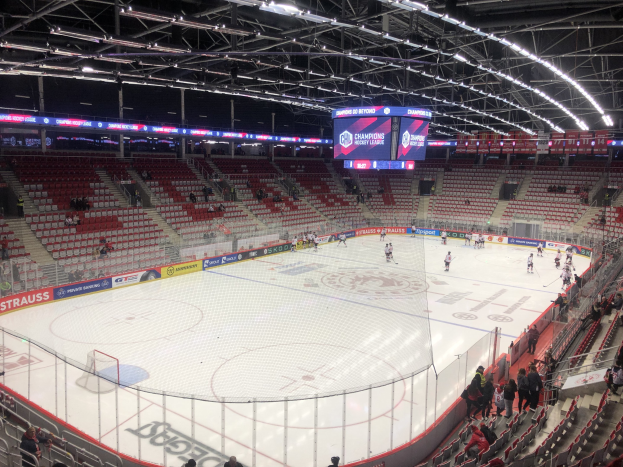 Eishockey-Spiel in einer großen Arena mit Zuschauern, eine von einem Zaun umgebene Eisfläche, ein Display mit "St. Louis Blues vs Detroit Red Wings" und Deckenbeleuchtung.