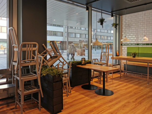 Innenansicht eines Berliner Restaurants mit hölzernen Tischen und Stühlen in der Nähe eines großen Fensters, das eine städtische Straße mit Fußgängern, Gebäuden und Straßenelementen zeigt.