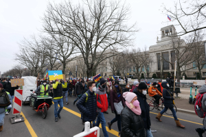 Eine große Gruppe von Menschen marschiert auf einer Straße in einer Demonstration, einige halten Schilder und Banner, andere fahren Fahrräder, mit Bäumen, Schildern und einem Gebäude im Hintergrund unter einem klaren blauen Himmel in Washington, D.C. am 21. Januar 2020.