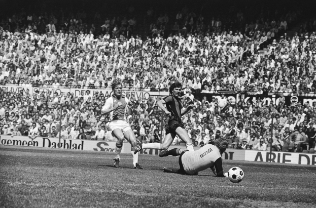 Schwarzes-Weiß-Foto von Fußballspielern im Einsatz auf einem Feld mit Zuschauern im Hintergrund und einem Banner mit der Aufschrift "Bundesliga 1978-79 Ajax 1-1 Hannover 96."