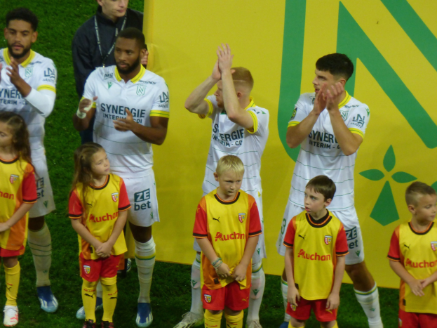 Eine Gruppe von Fußballspielern in Uniformen klatscht feierlich auf einem Ligue-1-Feld, mit einem "Ligue-1"-Schild im Hintergrund.