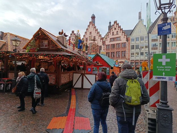 Menschen, die eine Kopfsteinpflasterstraße entlanggehen, neben einem Weihnachtsmarkt in Nürnberg, Deutschland, mit Laternenmasten und Informationsschildern im Vordergrund und Gebäuden im Hintergrund und einem bewölkten Himmel.