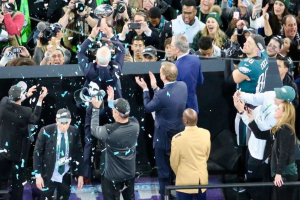 Philadelphia Eagles-Spieler feiern mit dem Vince Lombardi Trophy nach dem Sieg im Super Bowl, einige halten den Pokal und andere werfen Konfetti, mit einem Geländer und Fotografen im Hintergrund.