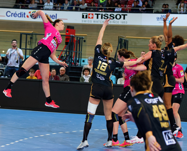 Frauen spielen Handball auf einem Feld mit einem Ball in der Luft, Zuschauer im Hintergrund und ein Schild mit der Aufschrift 'Futsal-Weltmeisterschaft 2019 - Bordeaux gegen Paris'.