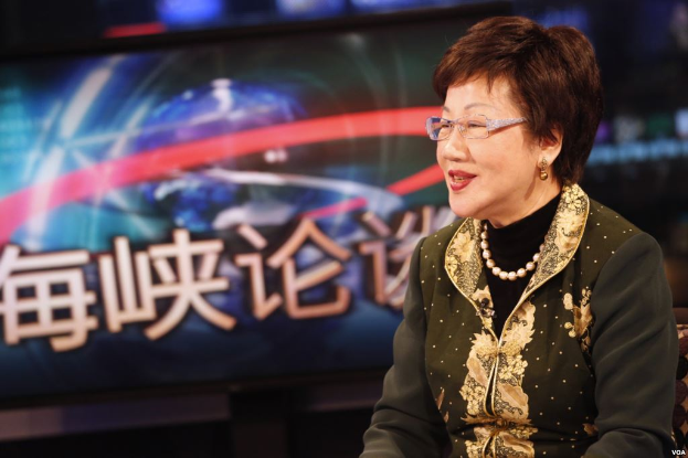 Eine Frau in einem schwarzen Kleid und Brille sitzt vor einem Fernseher