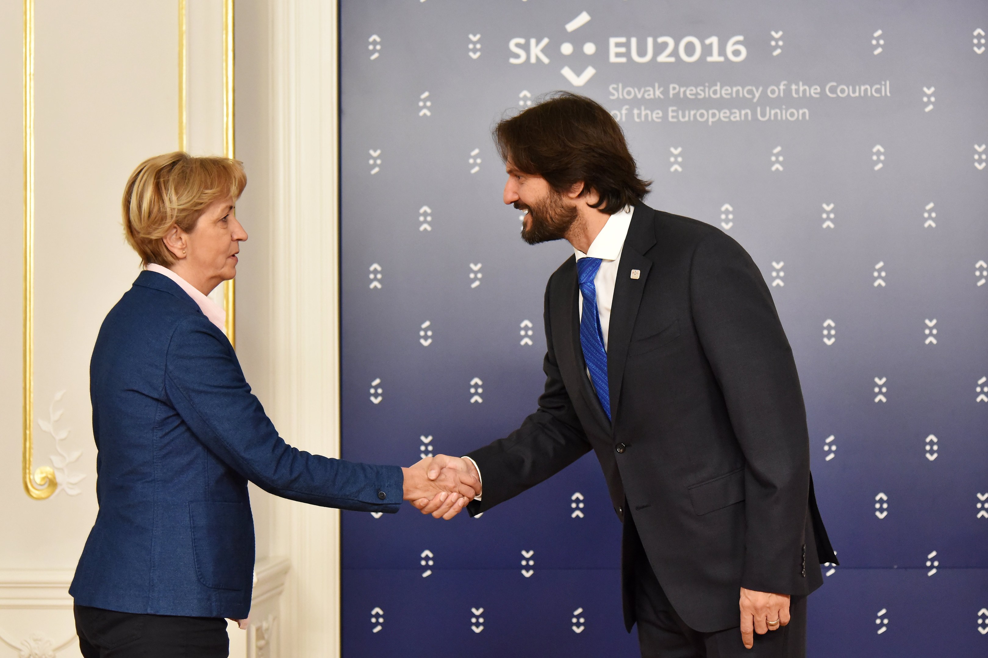 Bundeskanzlerin Angela Merkel und Bundespräsident Joachim Gauck schütteln sich lachend vor einer Wand mit einem "EU-Gipfel"-Schild und einer Tür die Hände.